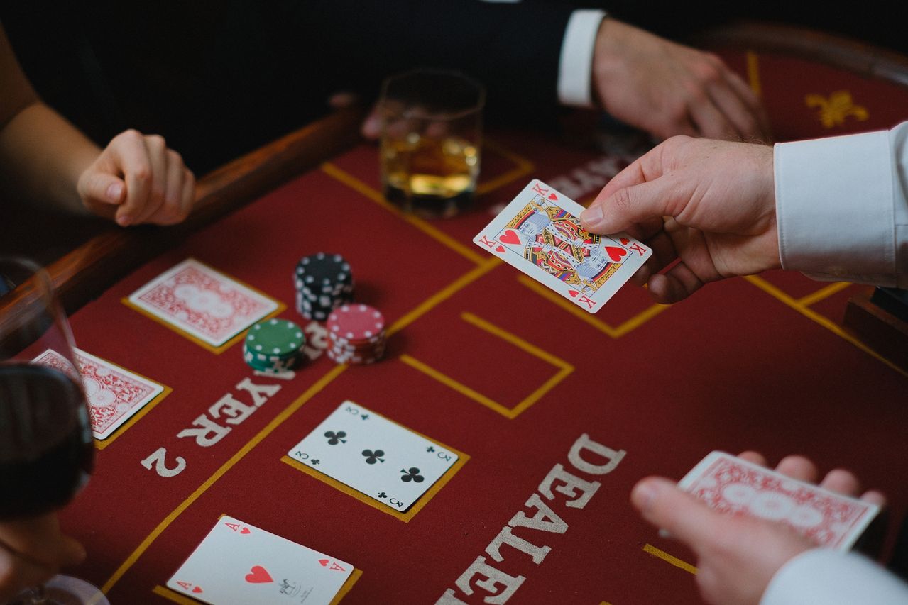 Guests and dealer at a red felt table with evening drinks